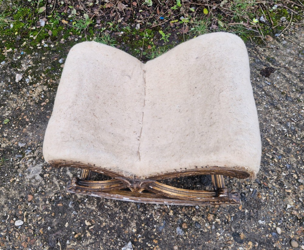 A late 19th-century giltwood rocking gout stool featuring a deeply curved cream fabric-upholstered seat supported by an ornate carved gilded frame. View IV