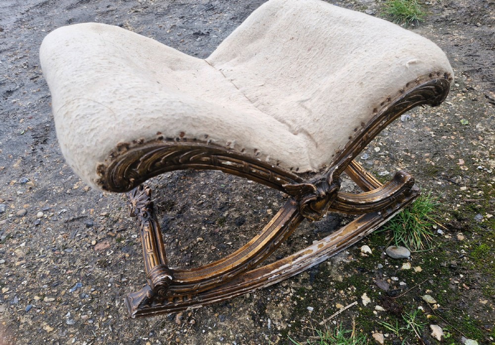 A late 19th-century giltwood rocking gout stool featuring a deeply curved cream fabric-upholstered seat supported by an ornate carved gilded frame. View VII