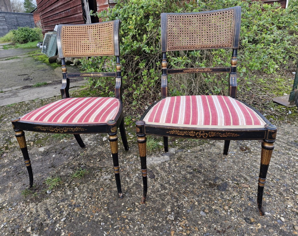 Pair of black painted antique side chairs featuring woven cane backrests, gold floral hand-painted details, and red and cream striped upholstered seats.