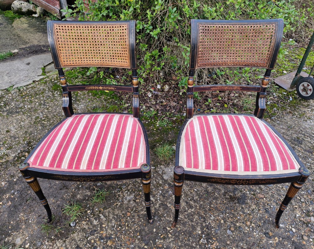 Pair of black painted antique side chairs featuring woven cane backrests, gold floral hand-painted details, and red and cream striped upholstered seats. View VI