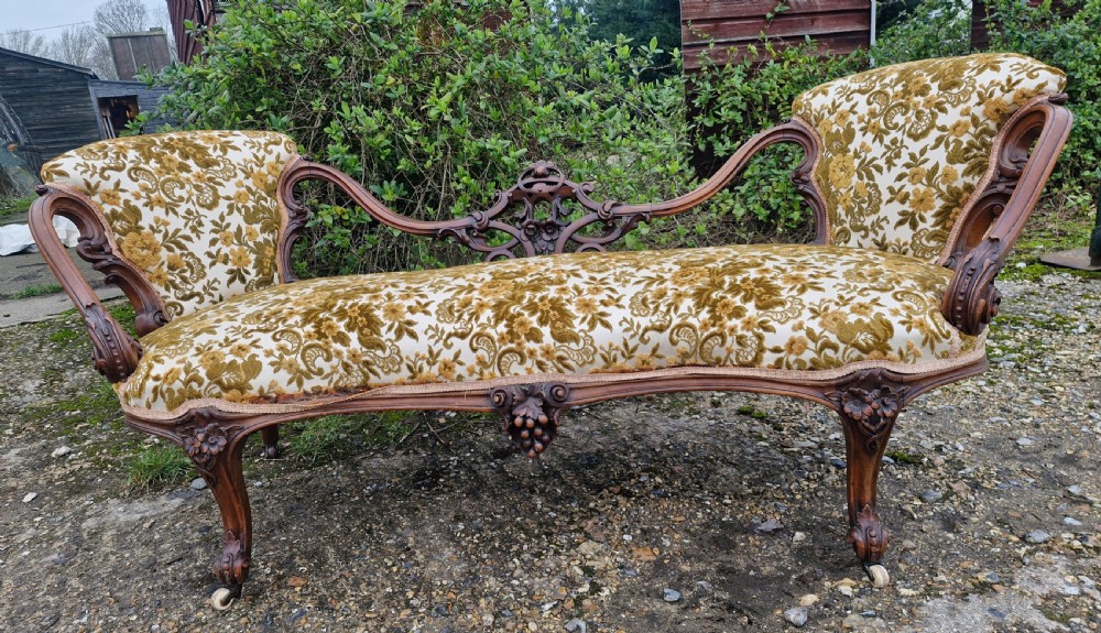 A Victorian carved walnut conversation seat featuring an S-shaped serpentine frame, floral patterned velvet upholstery, and carved cabriole legs on castors.