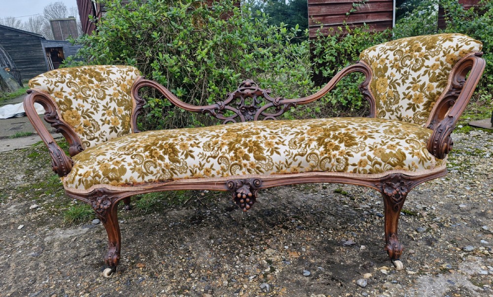 A Victorian carved walnut conversation seat featuring an S-shaped serpentine frame, floral patterned velvet upholstery, and carved cabriole legs on castors. View II