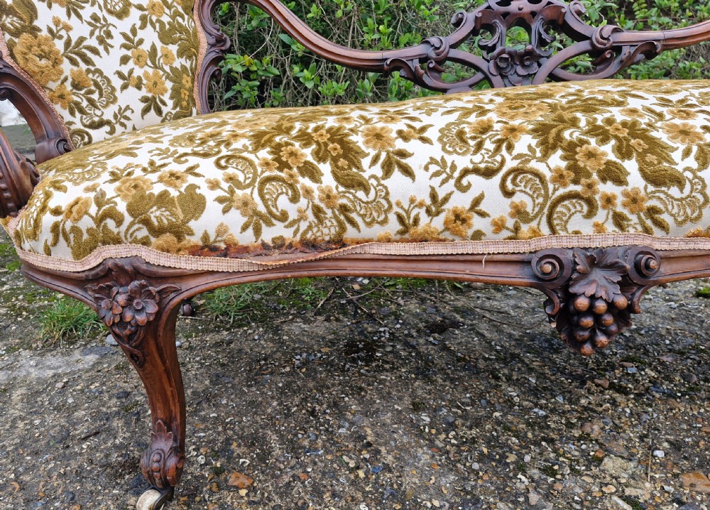 A Victorian carved walnut conversation seat featuring an S-shaped serpentine frame, floral patterned velvet upholstery, and carved cabriole legs on castors. View III