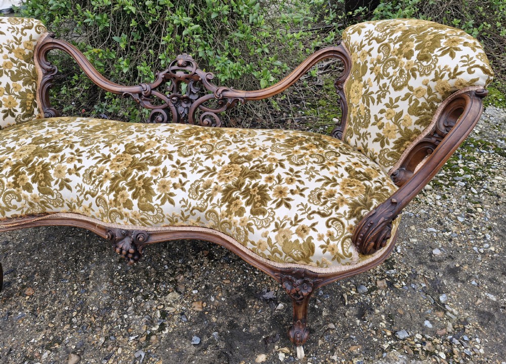 A Victorian carved walnut conversation seat featuring an S-shaped serpentine frame, floral patterned velvet upholstery, and carved cabriole legs on castors. View IV