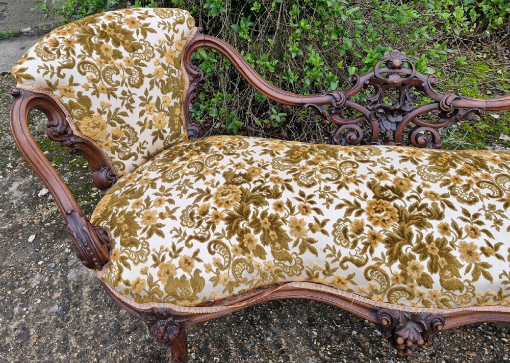 A Victorian carved walnut conversation seat featuring an S-shaped serpentine frame, floral patterned velvet upholstery, and carved cabriole legs on castors. View VII