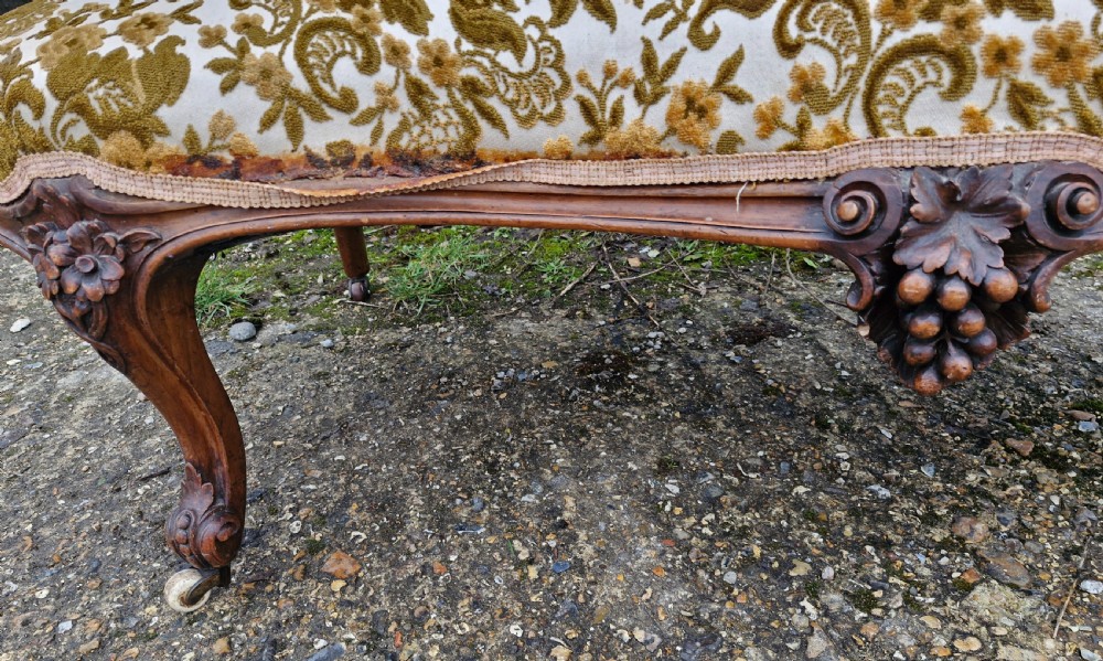 A Victorian carved walnut conversation seat featuring an S-shaped serpentine frame, floral patterned velvet upholstery, and carved cabriole legs on castors. View VIII