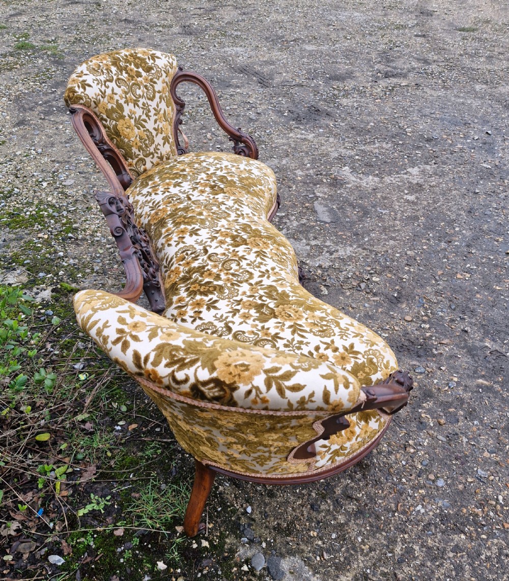 A Victorian carved walnut conversation seat featuring an S-shaped serpentine frame, floral patterned velvet upholstery, and carved cabriole legs on castors. View XIV
