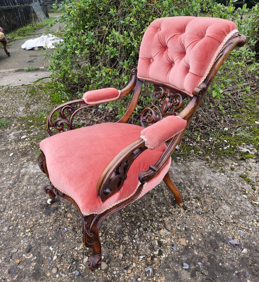 A Victorian carved walnut armchair upholstered in rose pink button-tufted velvet with pierced scrollwork detailing and cabriole legs.