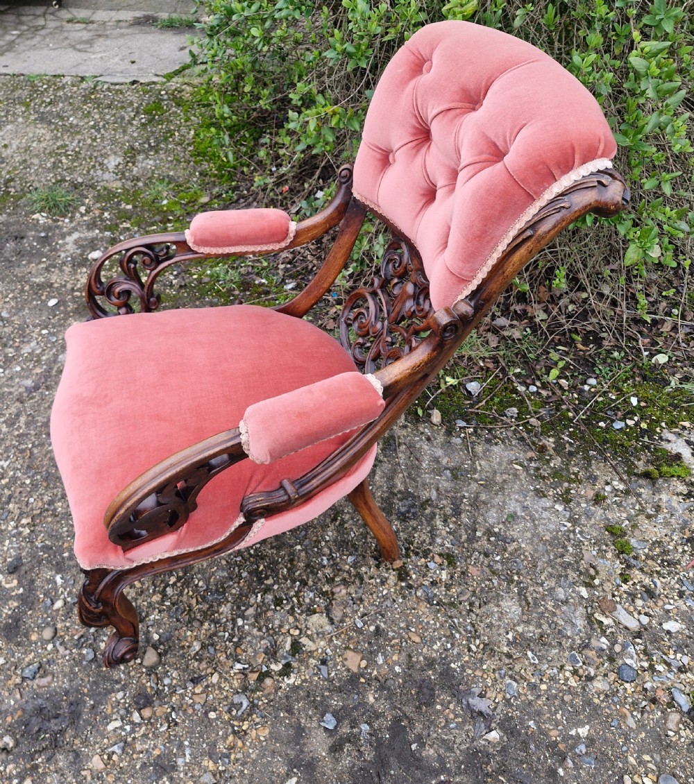 A Victorian carved walnut armchair upholstered in rose pink button-tufted velvet with pierced scrollwork detailing and cabriole legs. View V