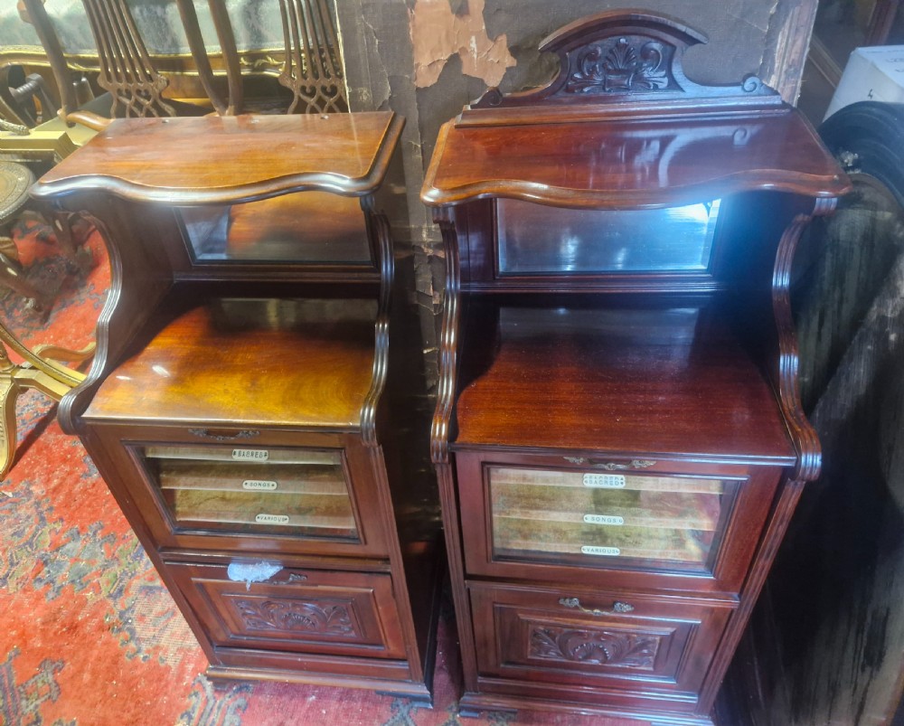 A matching pair of late Victorian dark mahogany music cabinets featuring upper mirrored shelves, glazed doors revealing labelled shelves, and lower carved wood panels. View VI