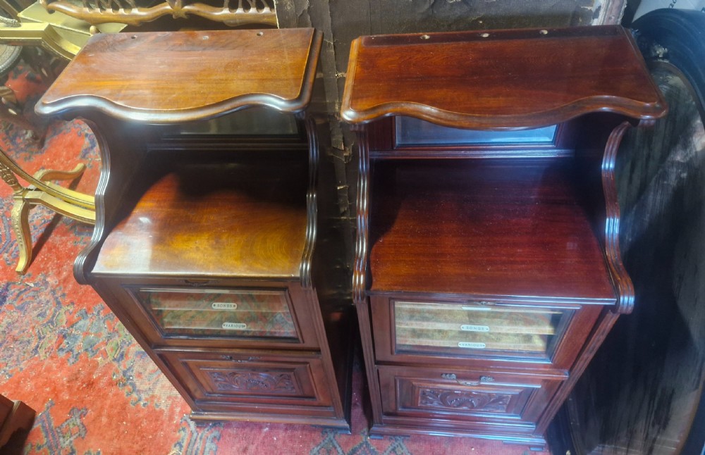 A matching pair of late Victorian dark mahogany music cabinets featuring upper mirrored shelves, glazed doors revealing labelled shelves, and lower carved wood panels. View IX