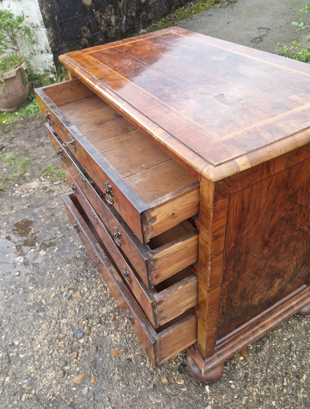 An antique walnut chest of four drawers featuring highly figured burr veneers, inlaid crossbanding, metal handles, and turned bun feet. View IV