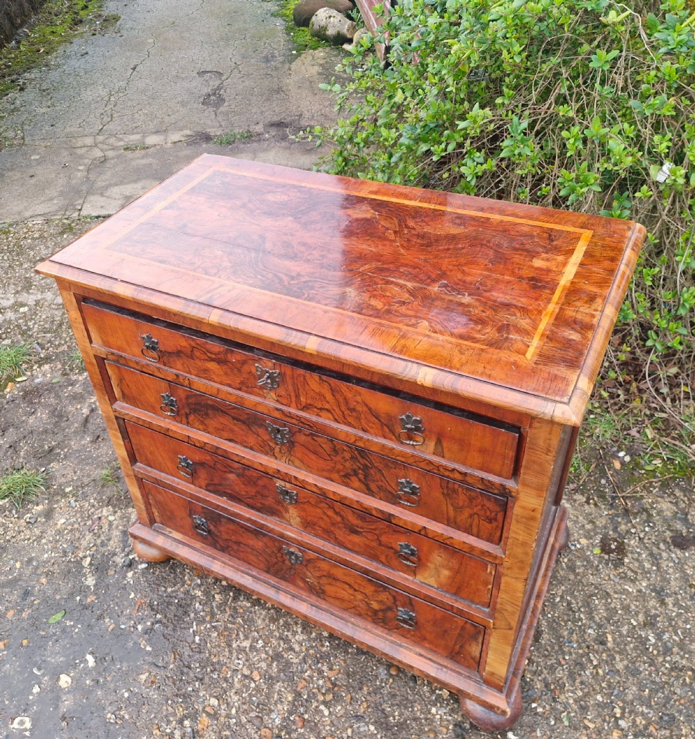 An antique walnut chest of four drawers featuring highly figured burr veneers, inlaid crossbanding, metal handles, and turned bun feet. View VII