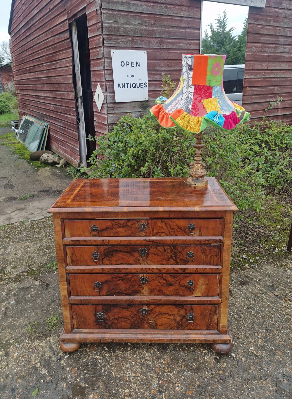 An antique walnut chest of four drawers featuring highly figured burr veneers, inlaid crossbanding, metal handles, and turned bun feet. View VIII