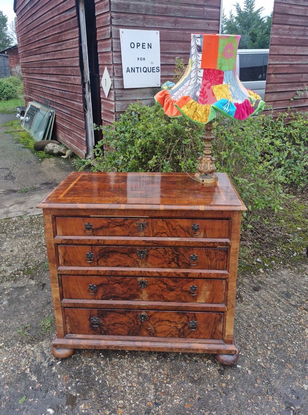 An antique walnut chest of four drawers featuring highly figured burr veneers, inlaid crossbanding, metal handles, and turned bun feet. View IX