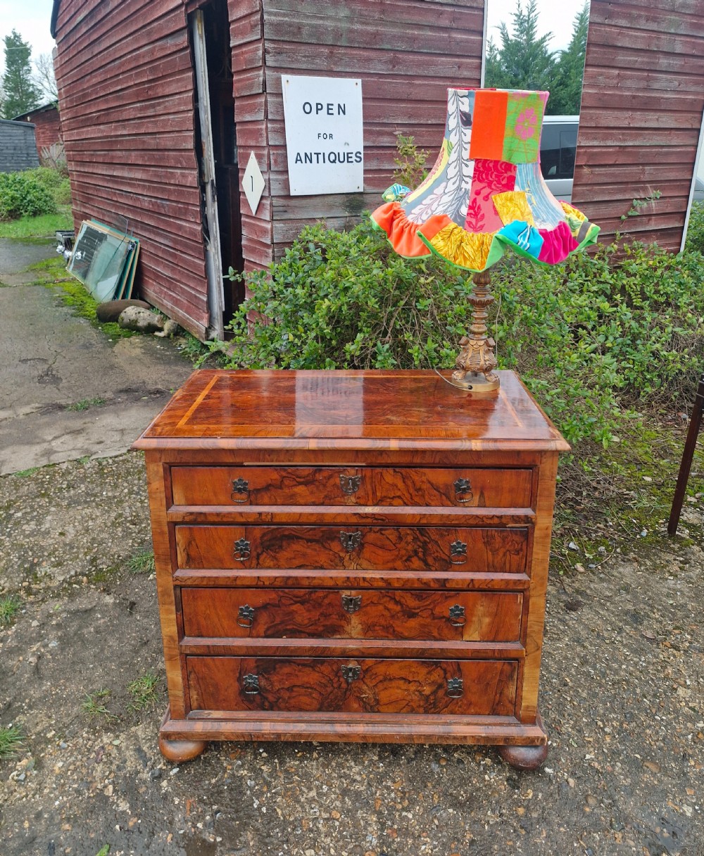 An antique walnut chest of four drawers featuring highly figured burr veneers, inlaid crossbanding, metal handles, and turned bun feet. View X