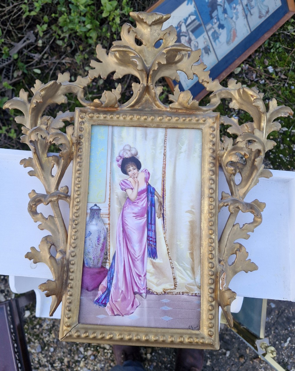 A late 19th-century rectangular hand-painted porcelain plaque depicting a woman in a pink gown inside an ornate carved gold giltwood frame.