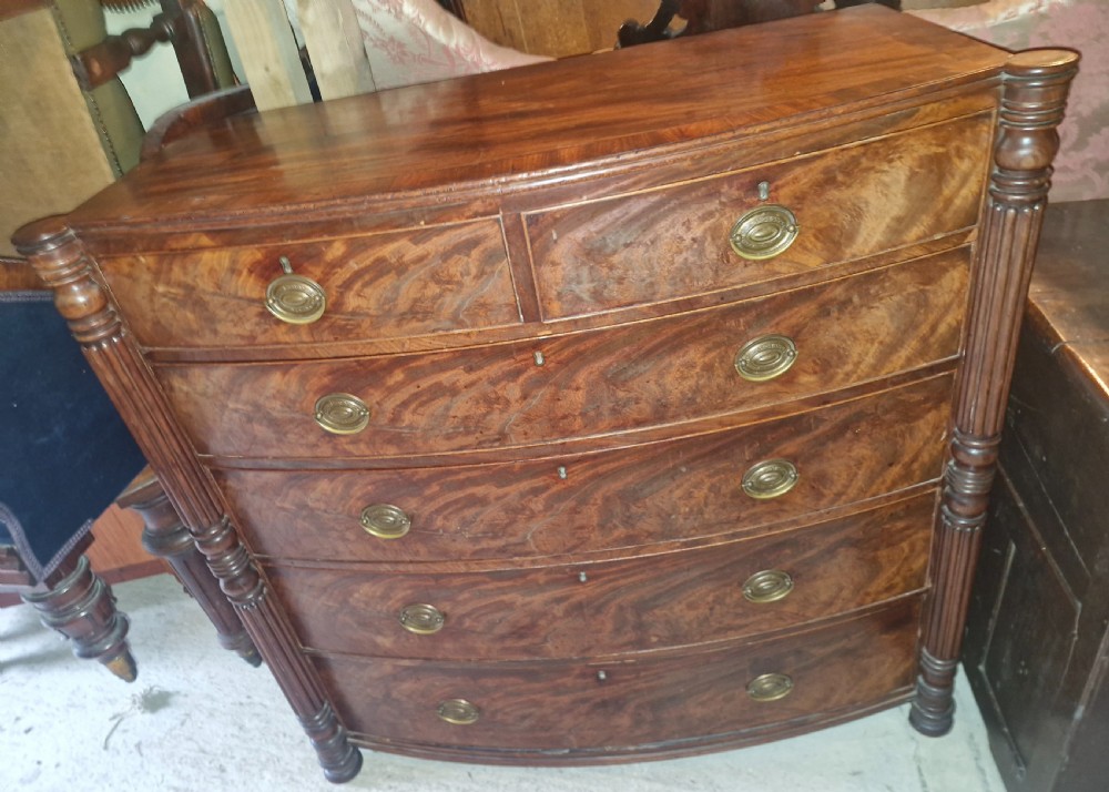 A Regency mahogany bow-front chest of drawers featuring two short over three long drawers with flame mahogany veneers, reeded side columns, and oval brass handles. View III