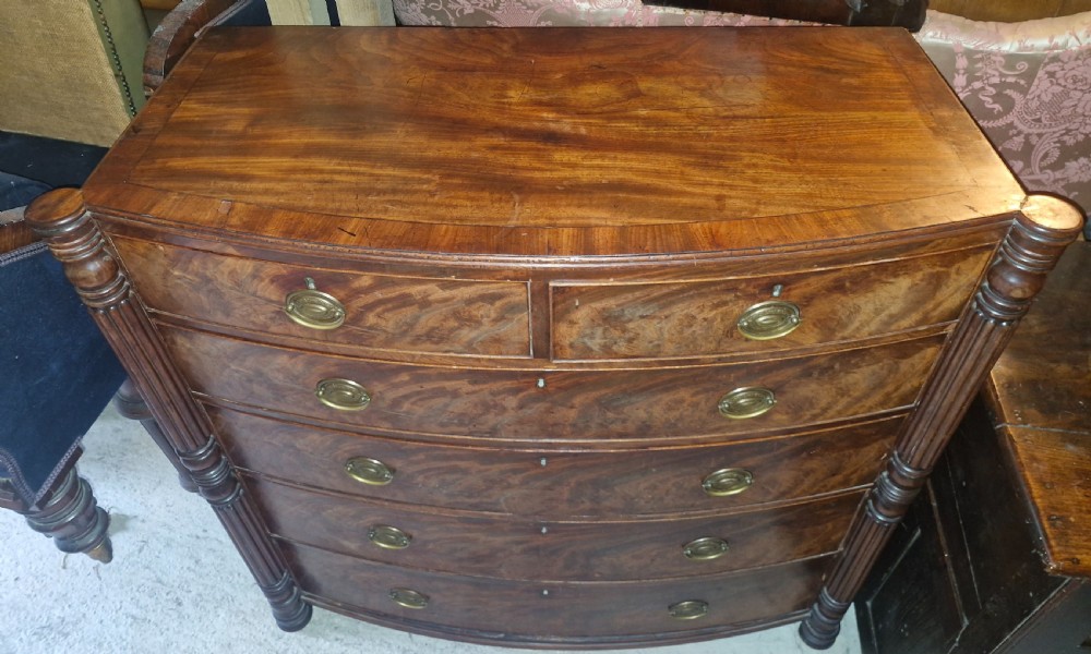 A Regency mahogany bow-front chest of drawers featuring two short over three long drawers with flame mahogany veneers, reeded side columns, and oval brass handles. View VII