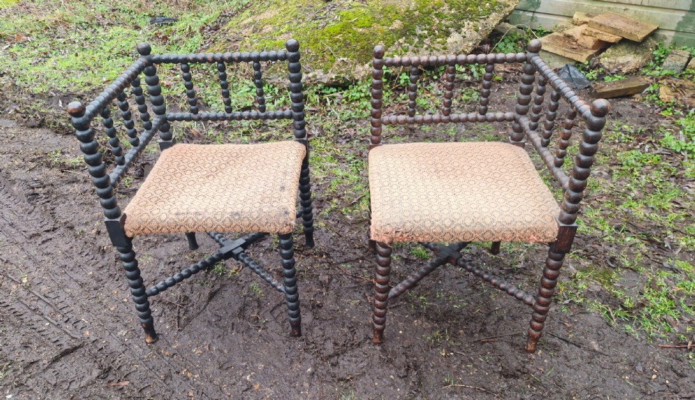 A pair of dark wood bobbin-turned corner chairs featuring patterned fabric seats and crossed lower stretchers.