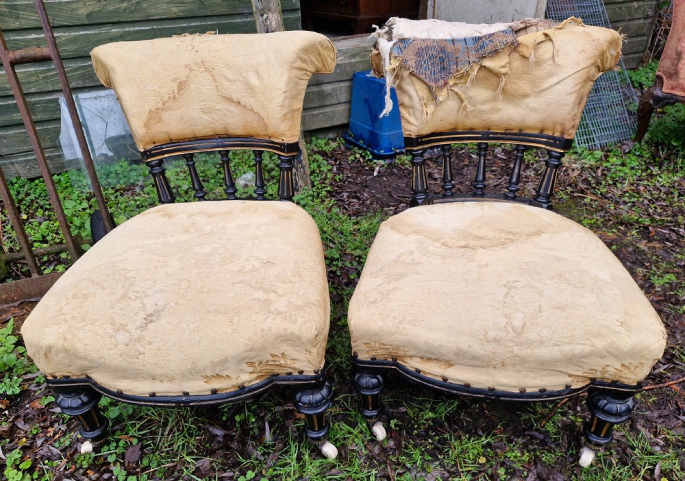 A pair of low Victorian ebonised nursing chairs with spindle backrests, turned front legs on ceramic castors, and worn yellow upholstery.
