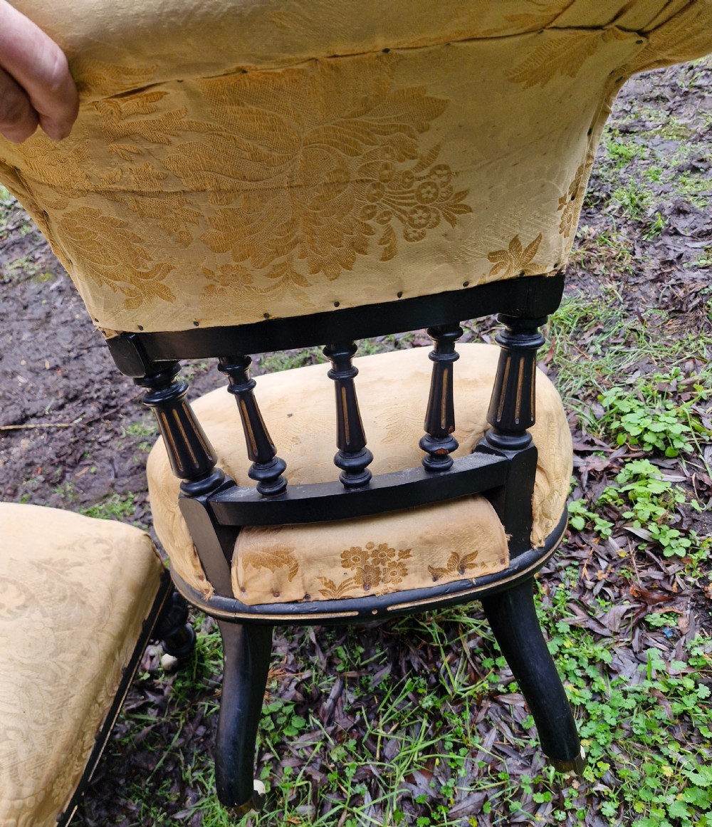 A pair of low Victorian ebonised nursing chairs with spindle backrests, turned front legs on ceramic castors, and worn yellow upholstery. View II