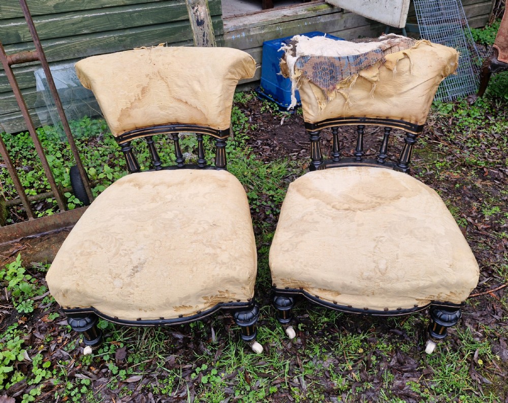 A pair of low Victorian ebonised nursing chairs with spindle backrests, turned front legs on ceramic castors, and worn yellow upholstery. View IV