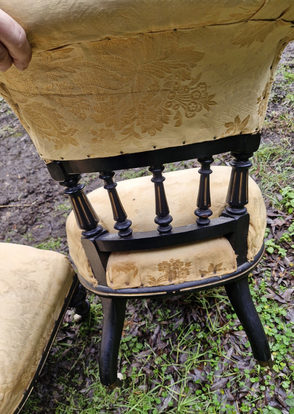 A pair of low Victorian ebonised nursing chairs with spindle backrests, turned front legs on ceramic castors, and worn yellow upholstery. View V