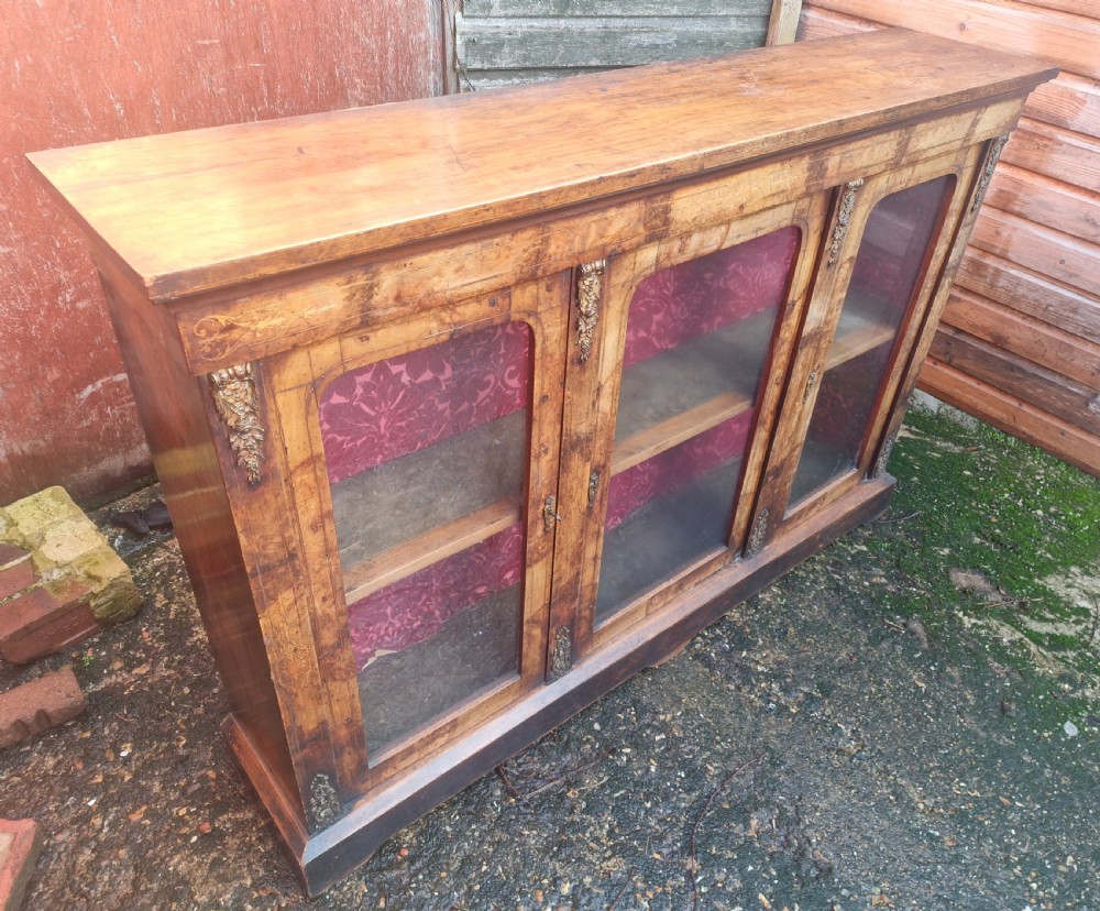 A nineteenth-century Victorian walnut side cabinet featuring three glazed glass doors with brass mounts and a red fabric lined interior.