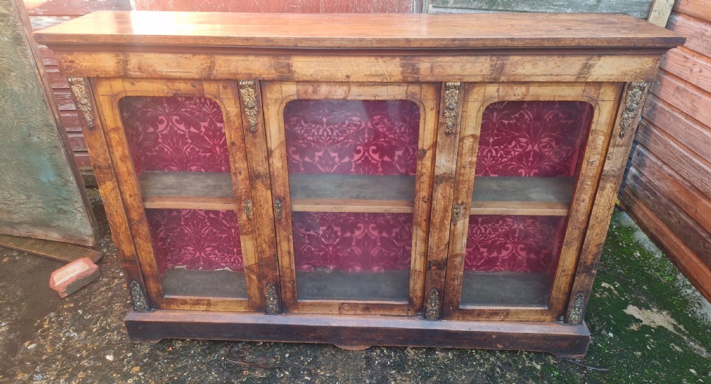 A nineteenth-century Victorian walnut side cabinet featuring three glazed glass doors with brass mounts and a red fabric lined interior. View V