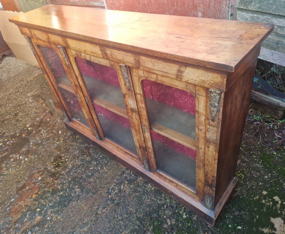 A nineteenth-century Victorian walnut side cabinet featuring three glazed glass doors with brass mounts and a red fabric lined interior. View VI