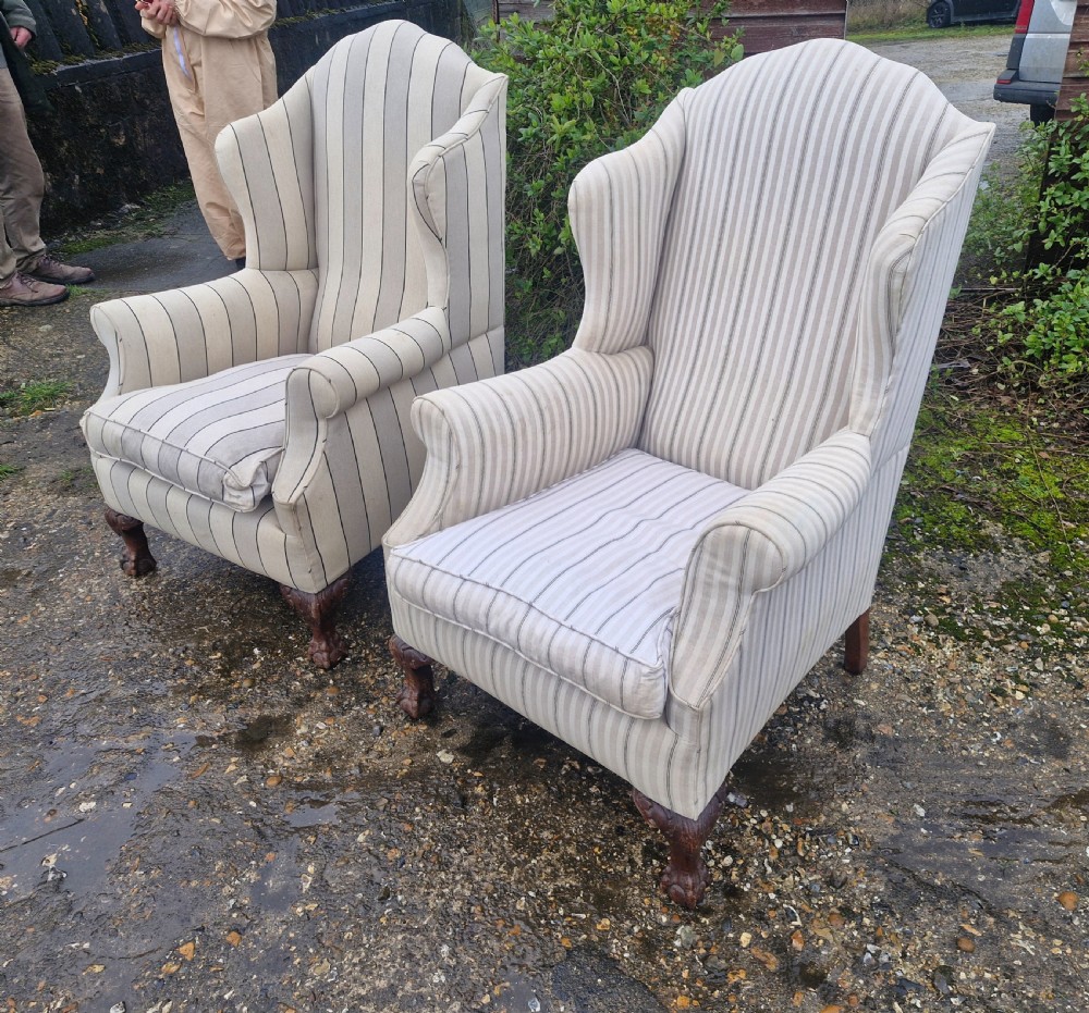 A pair of high-backed upholstered wingback armchairs featuring striped beige fabric and carved wooden cabriole legs with ball and claw feet.