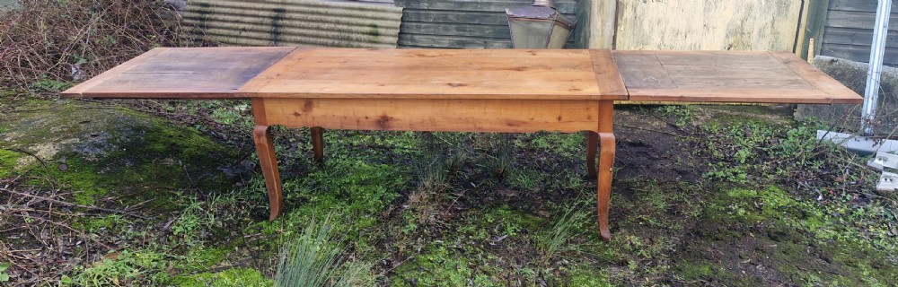 A long warm brown wooden French farmhouse dining table with two extended end leaves and curved cabriole legs.
