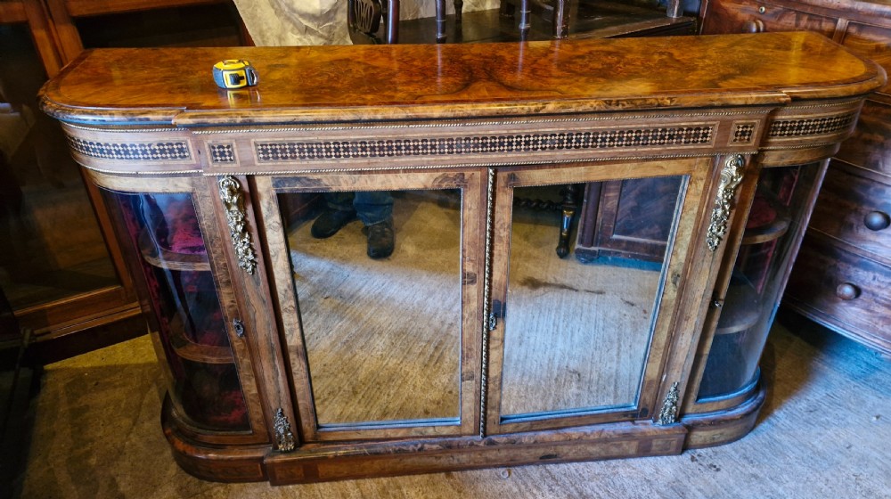 A 19th-century Victorian burr walnut credenza featuring geometric marquetry inlay, gilt metal mounts, central glass doors, and curved glass side display compartments.