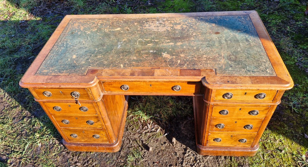 A Victorian walnut breakfront pedestal desk with a distressed green leather inset top and brass drop handles. View V
