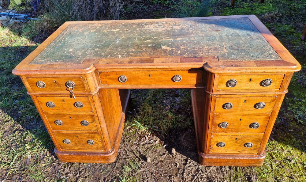 A Victorian walnut breakfront pedestal desk with a distressed green leather inset top and brass drop handles. View VI