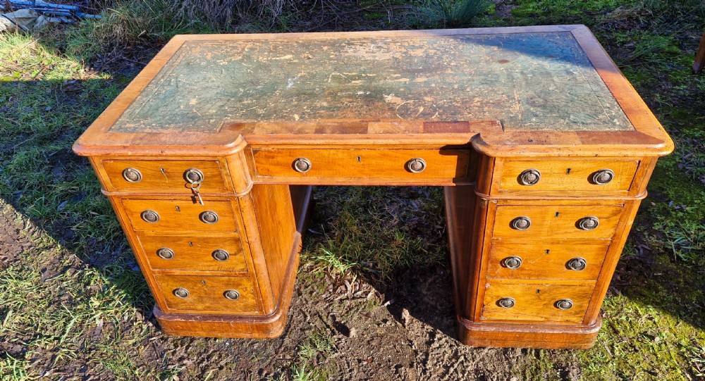 A Victorian walnut breakfront pedestal desk with a distressed green leather inset top and brass drop handles. View VII