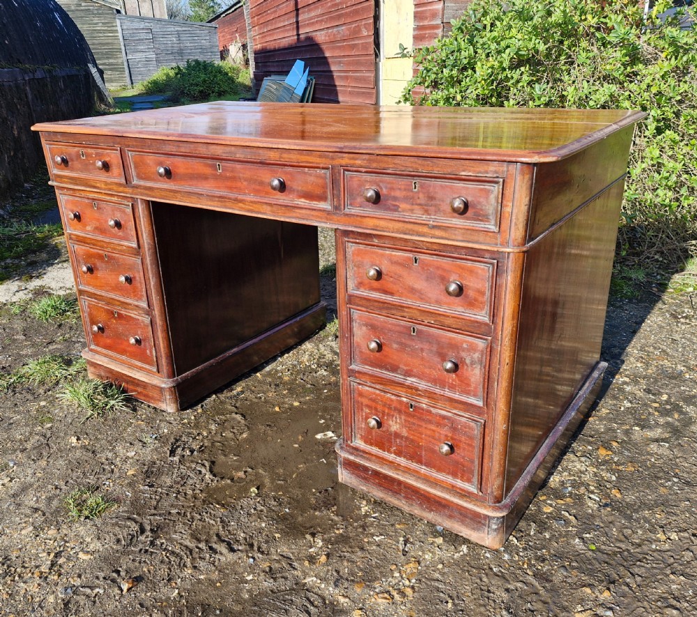 A Victorian mahogany pedestal writing desk with three top frieze drawers over twin pedestals, turned wooden knobs, and a plinth base.