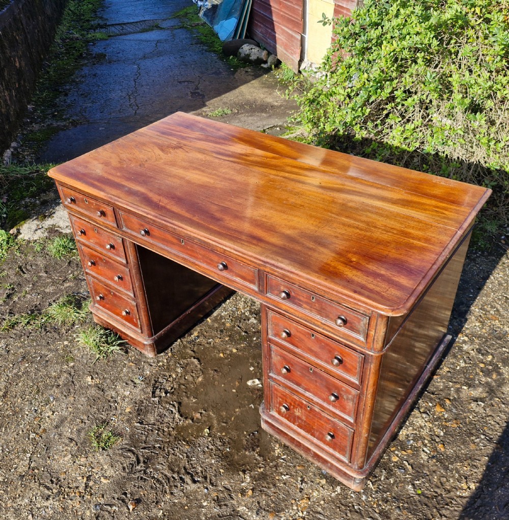 A Victorian mahogany pedestal writing desk with three top frieze drawers over twin pedestals, turned wooden knobs, and a plinth base. View V