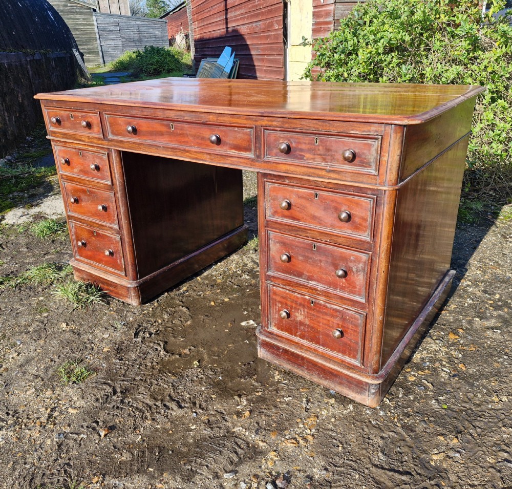 A Victorian mahogany pedestal writing desk with three top frieze drawers over twin pedestals, turned wooden knobs, and a plinth base. View VI