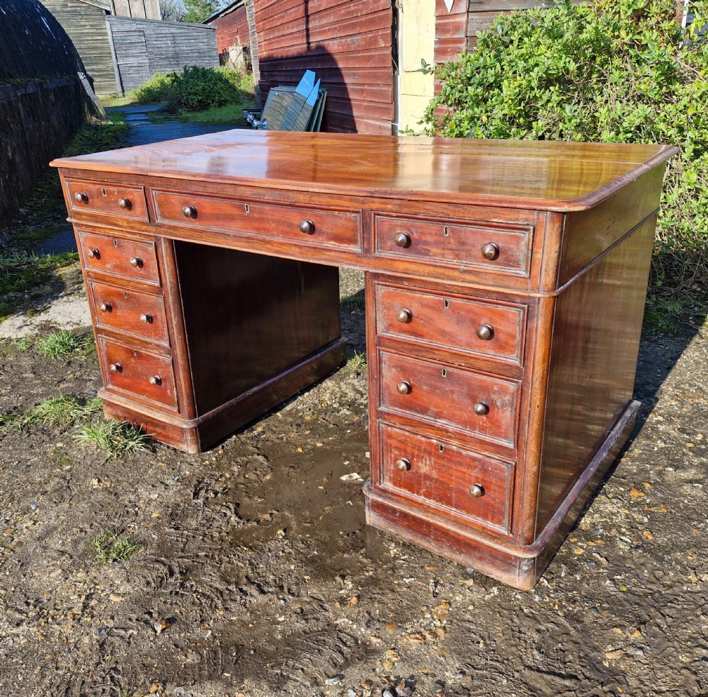 A Victorian mahogany pedestal writing desk with three top frieze drawers over twin pedestals, turned wooden knobs, and a plinth base. View VII