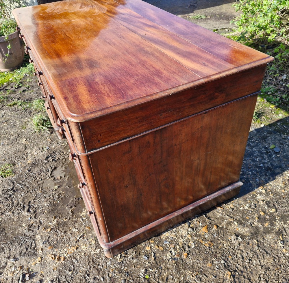 A Victorian mahogany pedestal writing desk with three top frieze drawers over twin pedestals, turned wooden knobs, and a plinth base. View IX