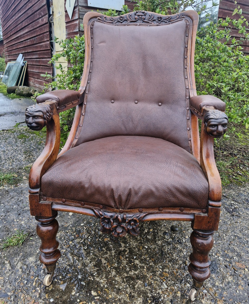 A mid-19th century carved mahogany library armchair upholstered in brown leather, featuring carved lion heads on the armrest terminals and turned legs with castors.