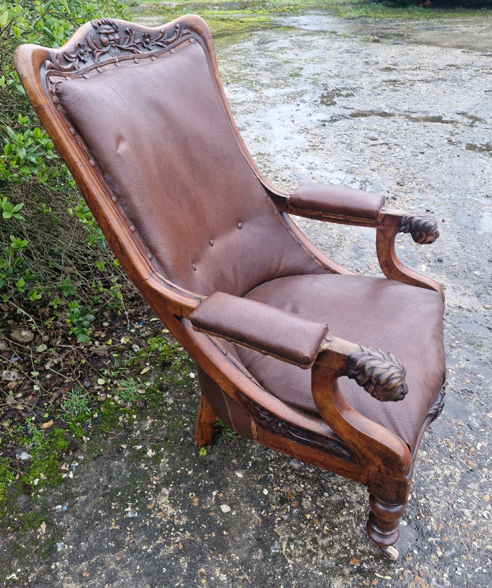 A mid-19th century carved mahogany library armchair upholstered in brown leather, featuring carved lion heads on the armrest terminals and turned legs with castors. View IX