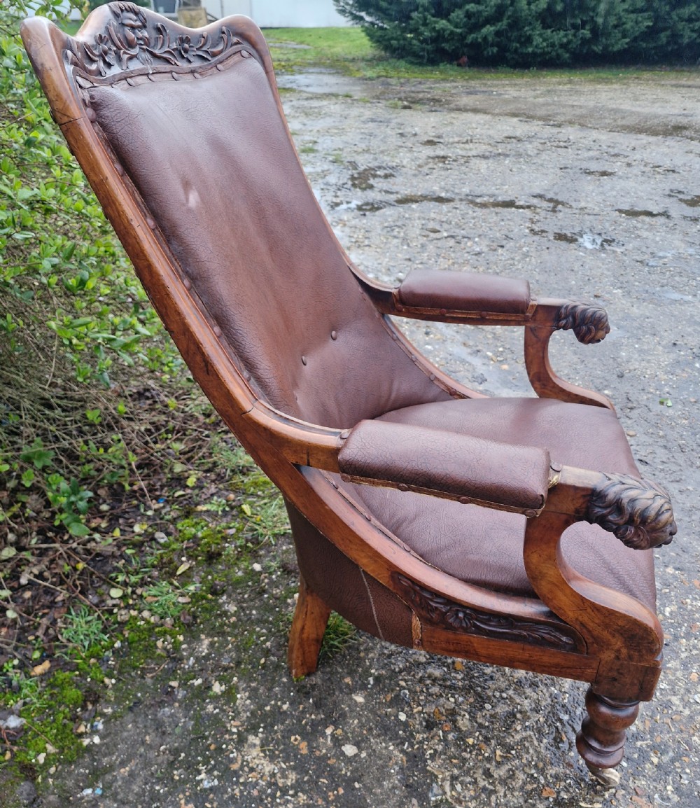A mid-19th century carved mahogany library armchair upholstered in brown leather, featuring carved lion heads on the armrest terminals and turned legs with castors. View X