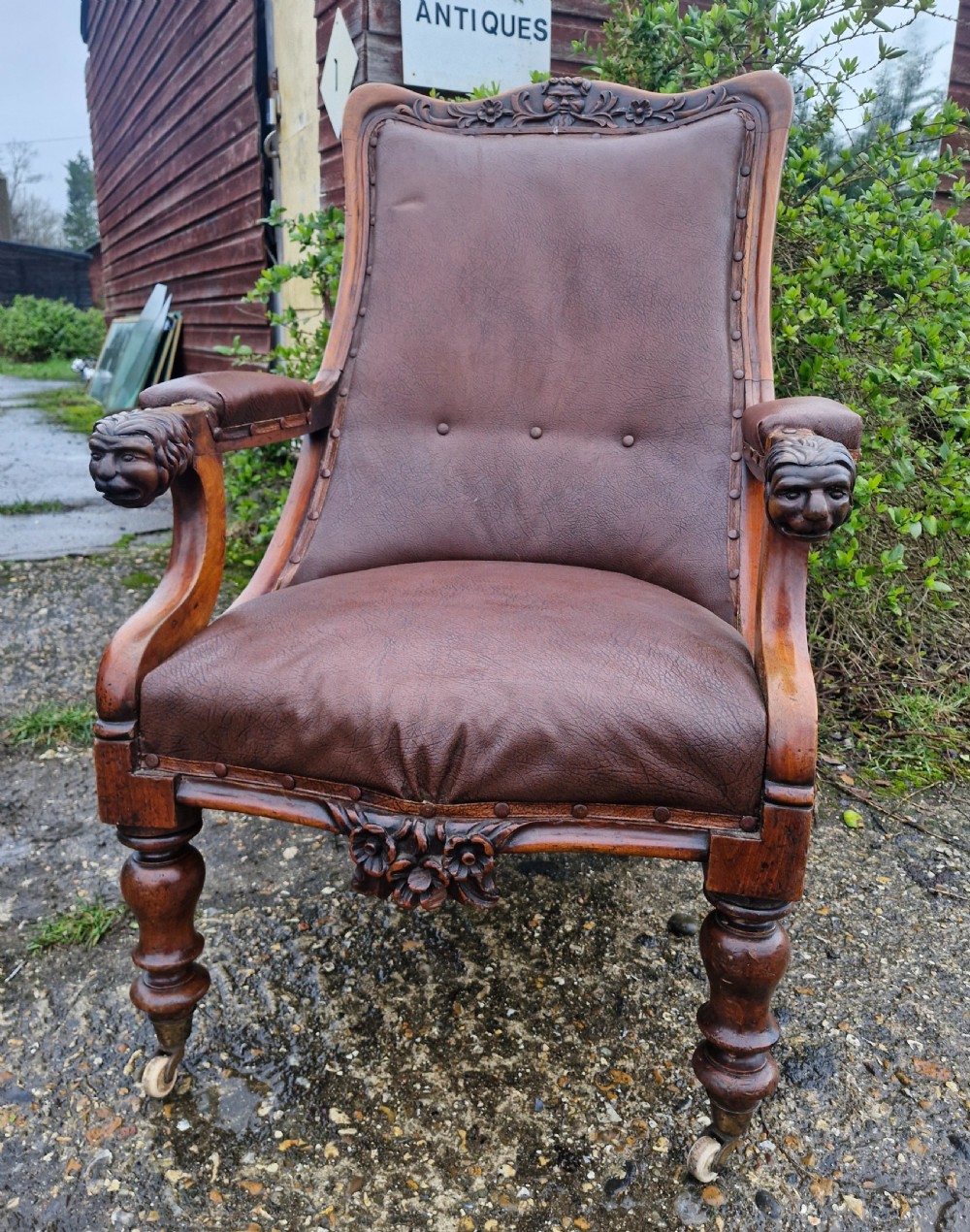 A mid-19th century carved mahogany library armchair upholstered in brown leather, featuring carved lion heads on the armrest terminals and turned legs with castors. View XI