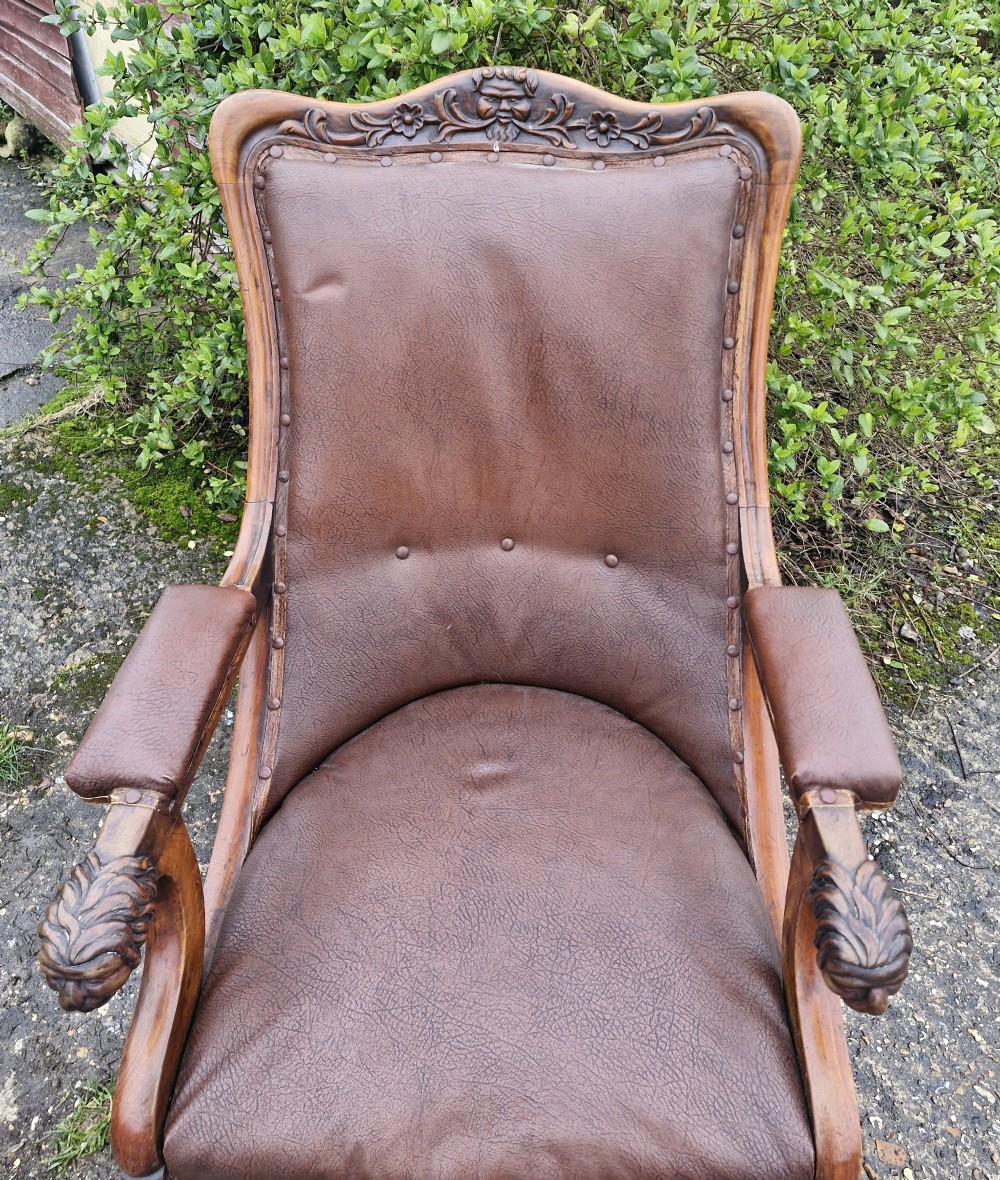 A mid-19th century carved mahogany library armchair upholstered in brown leather, featuring carved lion heads on the armrest terminals and turned legs with castors. View V
