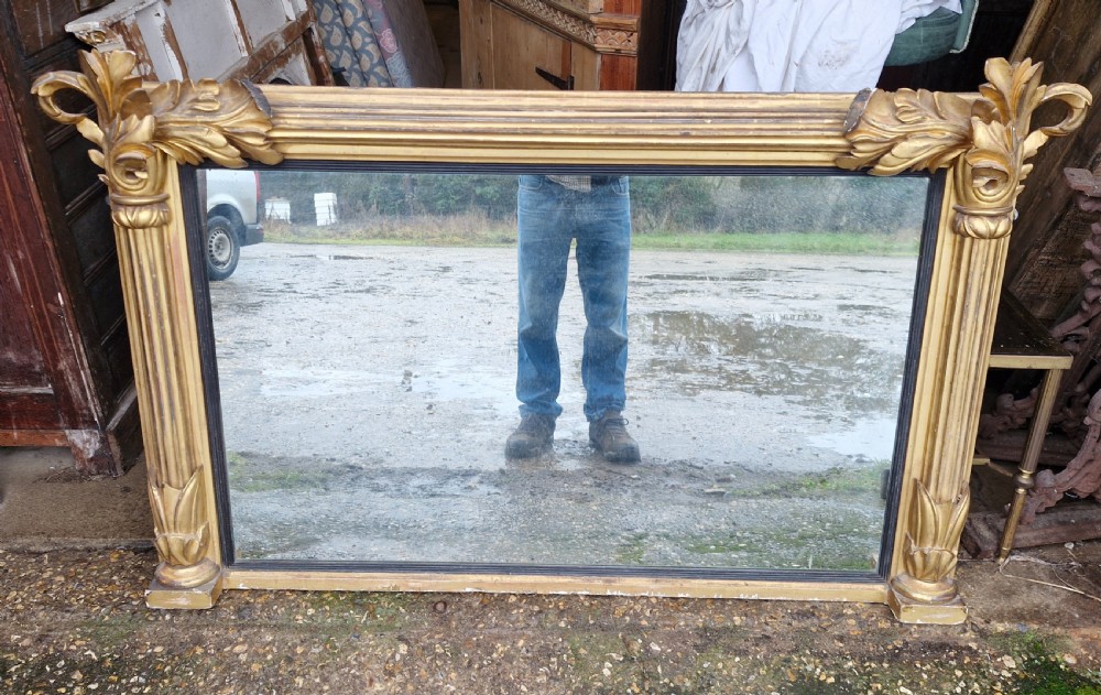 A wide rectangular Regency giltwood overmantel mirror featuring carved acanthus leaf corner details, fluted side columns, and an ebonised inner border. View III
