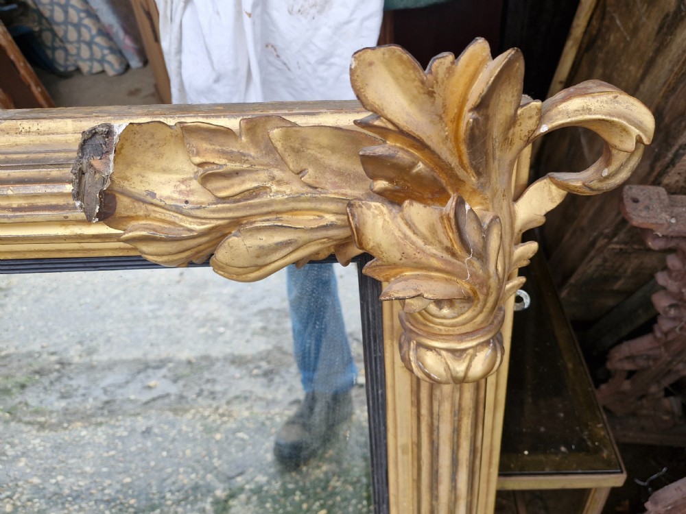 A wide rectangular Regency giltwood overmantel mirror featuring carved acanthus leaf corner details, fluted side columns, and an ebonised inner border. View IV