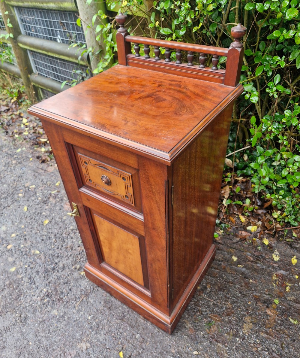 A late Victorian mahogany bedside cabinet featuring a spindle gallery top, a carved fielded door panel, and a brass latch. View V